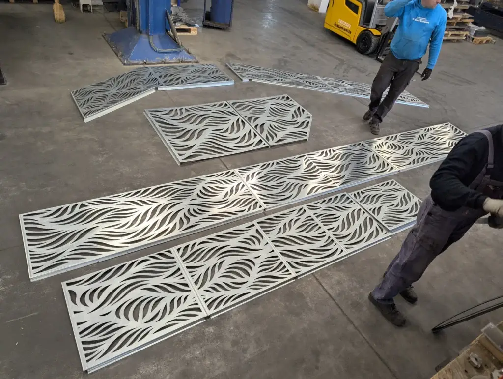 Aluminium lézervágott panelek gyártói csarnokban a földre fektetve egymáshoz illesztve porfestés előtt, nyersen.